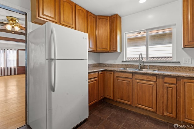 kitchen with brown cabinetry, freestanding refrigerator, a sink, and a ceiling fan