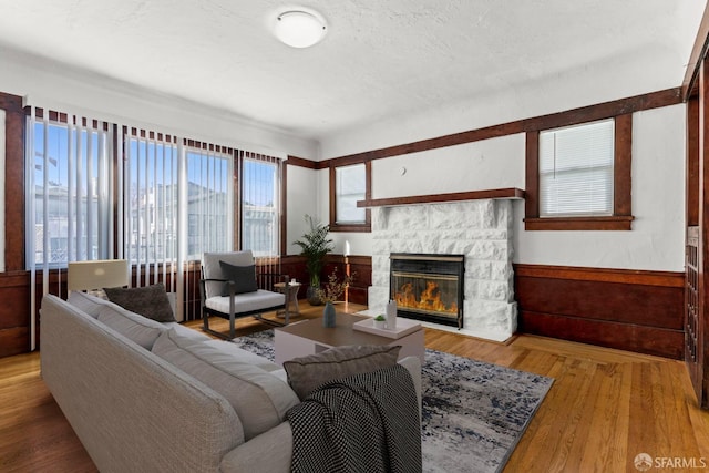 living room featuring a textured ceiling, wood finished floors, and a stone fireplace