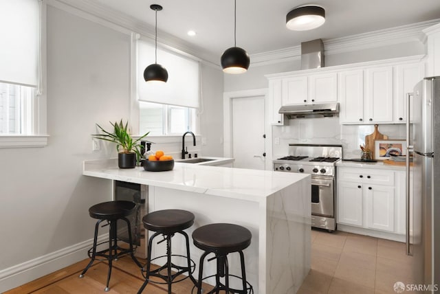 kitchen with sink, appliances with stainless steel finishes, kitchen peninsula, pendant lighting, and white cabinets