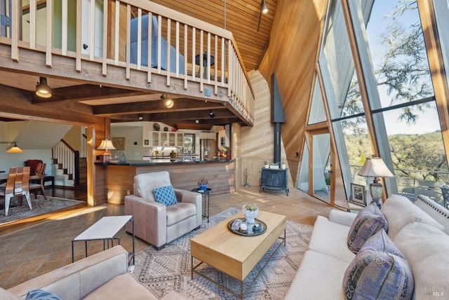 living area with wood walls, stairs, wooden ceiling, a wood stove, and a towering ceiling
