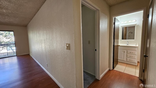 hallway with sink, a textured ceiling, and light wood-type flooring