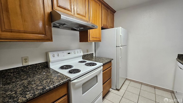 kitchen featuring dark stone countertops, light tile patterned floors, and white appliances