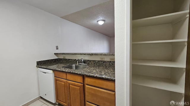 kitchen featuring sink, dishwasher, a textured ceiling, light tile patterned flooring, and dark stone counters