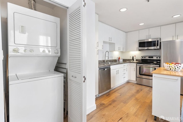 kitchen with white cabinetry, sink, stainless steel appliances, and stacked washer / dryer