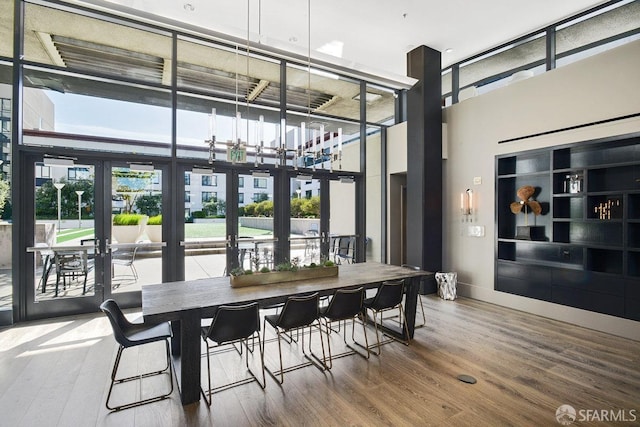 dining area featuring a high ceiling, wood-type flooring, floor to ceiling windows, and french doors