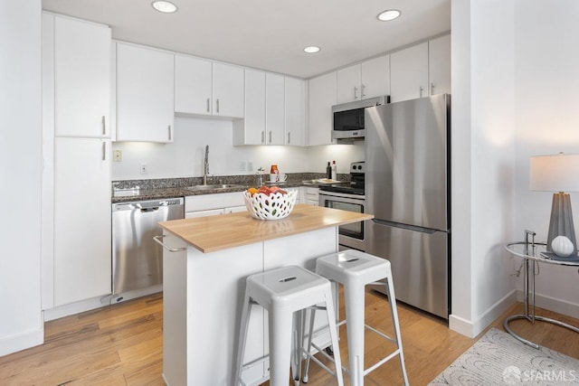 kitchen with a breakfast bar, sink, white cabinets, stainless steel appliances, and light wood-type flooring