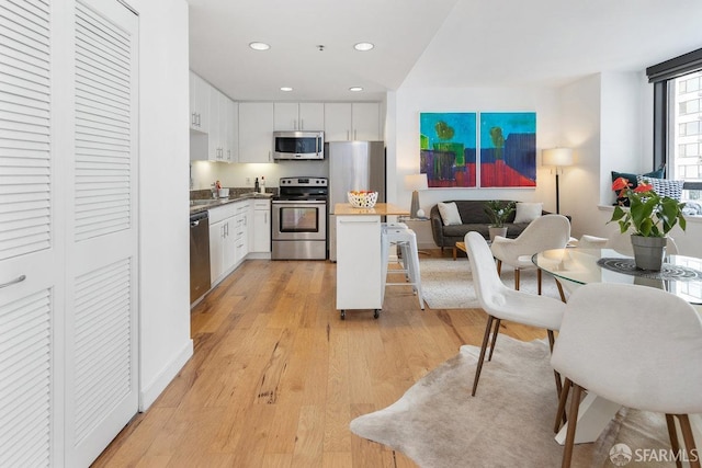 kitchen featuring appliances with stainless steel finishes, light wood-type flooring, white cabinets, and a kitchen bar