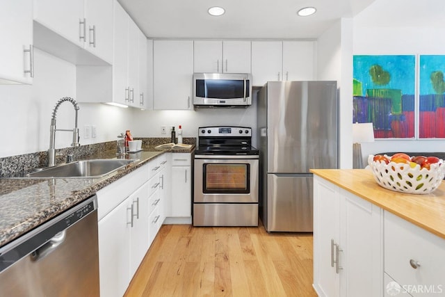 kitchen featuring appliances with stainless steel finishes, white cabinetry, sink, dark stone counters, and light wood-type flooring