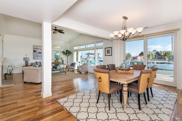 dining area with ornamental molding, vaulted ceiling, light wood-type flooring, baseboards, and ceiling fan with notable chandelier