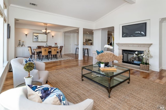 living area with ornamental molding, a glass covered fireplace, wood finished floors, and visible vents