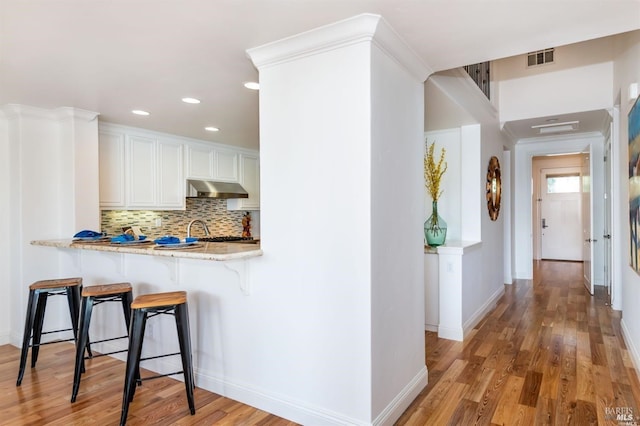 kitchen with light wood-type flooring, under cabinet range hood, a kitchen bar, and decorative backsplash