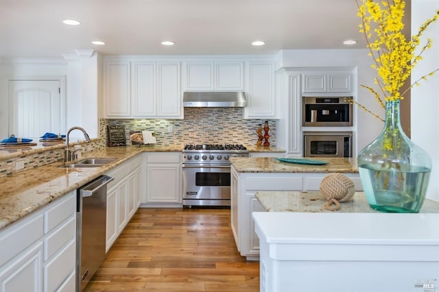 kitchen with light wood finished floors, stainless steel appliances, under cabinet range hood, white cabinetry, and a sink