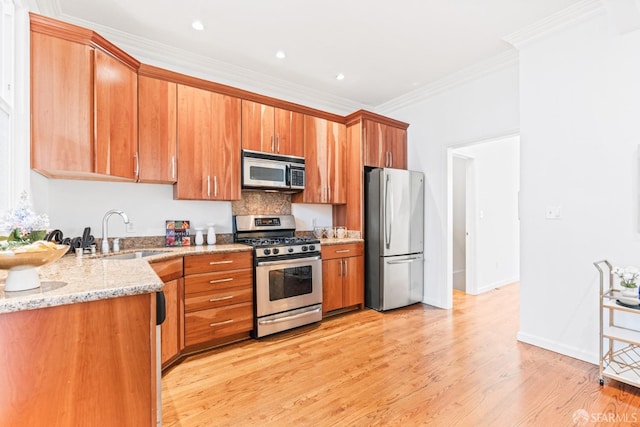 kitchen featuring light wood-style floors, light stone countertops, ornamental molding, a sink, and stainless steel appliances