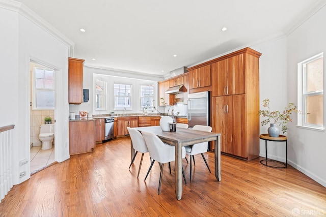 kitchen with light wood-style flooring, under cabinet range hood, brown cabinetry, appliances with stainless steel finishes, and a sink