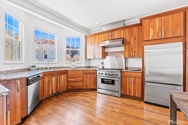 kitchen featuring crown molding, light wood-style flooring, high end appliances, under cabinet range hood, and a sink