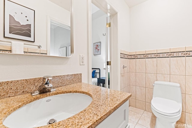 bathroom featuring toilet, tile walls, vanity, wainscoting, and tile patterned flooring