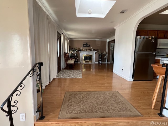 hallway featuring visible vents, a skylight, crown molding, arched walkways, and light wood-style floors