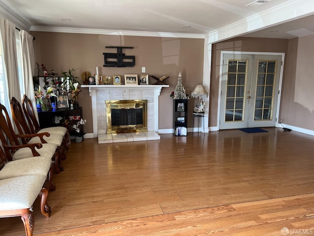 living area featuring crown molding, a tiled fireplace, french doors, wood finished floors, and baseboards