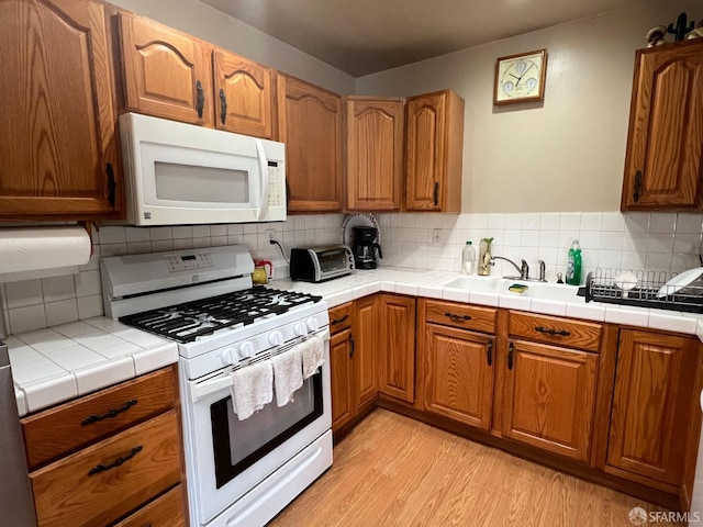 kitchen featuring tile countertops, light wood-type flooring, brown cabinetry, white appliances, and decorative backsplash