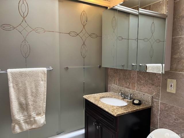 bathroom with tile walls, toilet, vanity, an enclosed shower, and backsplash