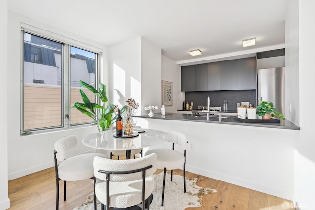 kitchen featuring tasteful backsplash, kitchen peninsula, light hardwood / wood-style flooring, and stainless steel refrigerator