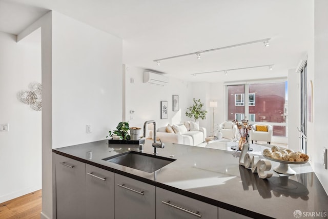 kitchen with sink, a wall mounted AC, track lighting, gray cabinets, and light wood-type flooring