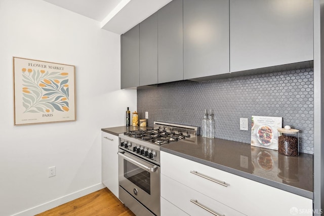 kitchen with high end range, backsplash, gray cabinetry, dark stone countertops, and light hardwood / wood-style floors