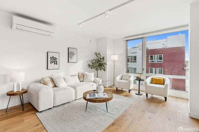 living room featuring an AC wall unit, rail lighting, and light hardwood / wood-style flooring