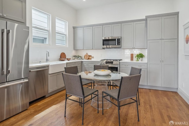 3511 23rd St Unit 1, San Francisco, CA 94110 - kitchen featuring stainless steel appliances, gray cabinetry, light wood-style floors, tasteful backsplash, and light countertops