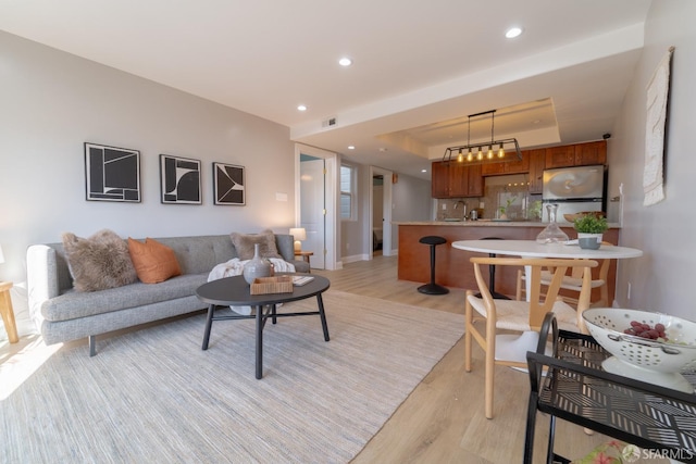 living room featuring sink, a tray ceiling, and light hardwood / wood-style flooring