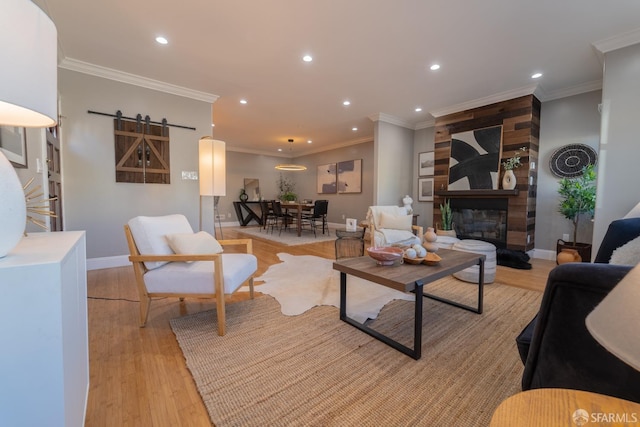 living room featuring a large fireplace, ornamental molding, a barn door, and light hardwood / wood-style floors