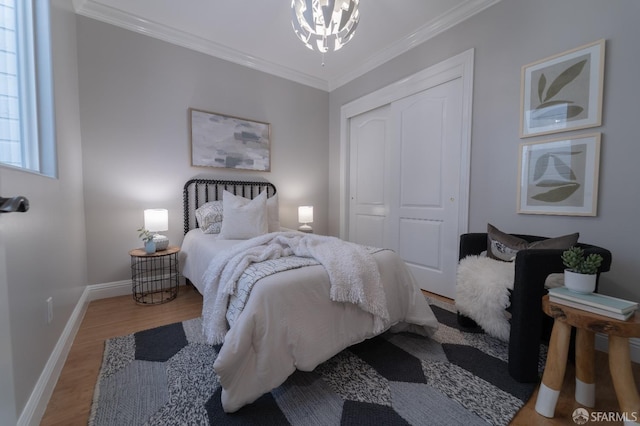 bedroom featuring a notable chandelier, hardwood / wood-style flooring, ornamental molding, and a closet