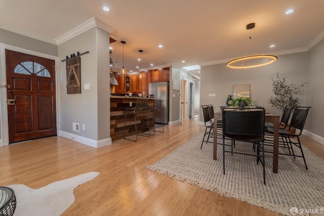 dining room with ornamental molding, a barn door, and light wood-type flooring