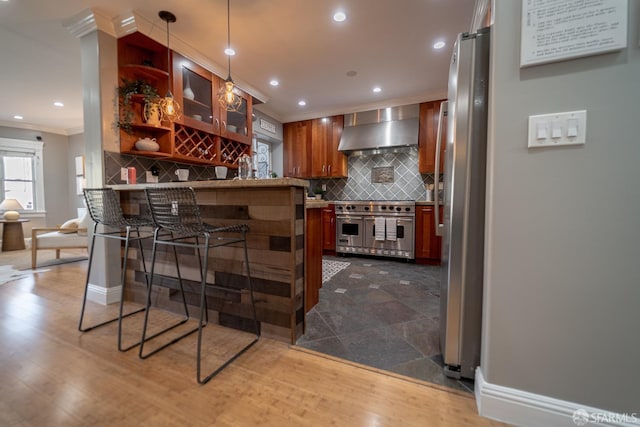 bar featuring tasteful backsplash, ornamental molding, appliances with stainless steel finishes, and wall chimney range hood