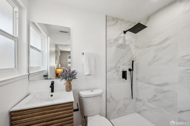 bathroom featuring toilet, vanity, visible vents, and tiled shower