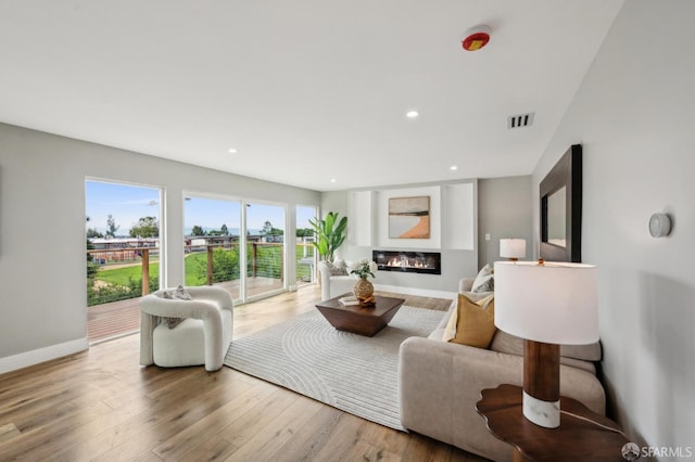 living room featuring baseboards, visible vents, recessed lighting, a glass covered fireplace, and wood finished floors