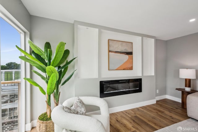 living area featuring recessed lighting, a glass covered fireplace, wood finished floors, and baseboards