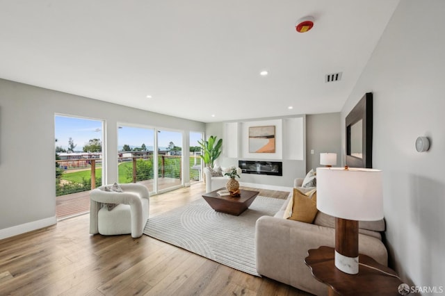 living area with baseboards, visible vents, a glass covered fireplace, recessed lighting, and wood finished floors