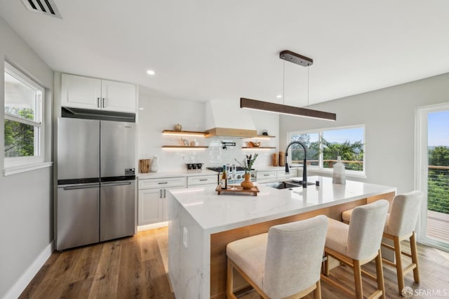 kitchen with visible vents, a sink, premium range hood, freestanding refrigerator, and light wood-style floors