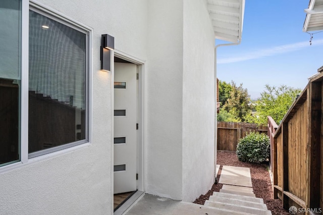 view of exterior entry featuring stucco siding and fence