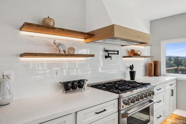 kitchen with open shelves, stainless steel range, premium range hood, backsplash, and white cabinetry