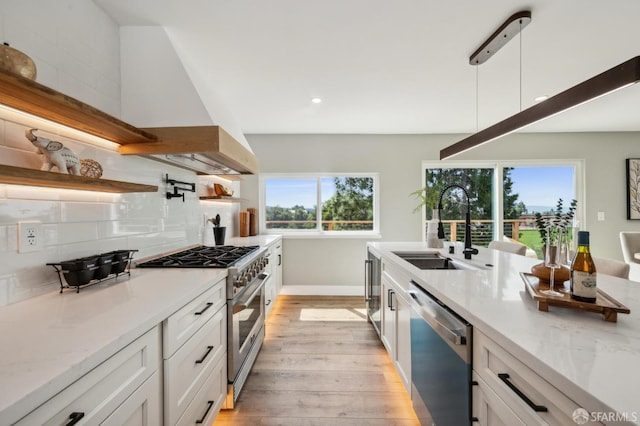 kitchen featuring ventilation hood, light wood finished floors, a sink, decorative backsplash, and appliances with stainless steel finishes