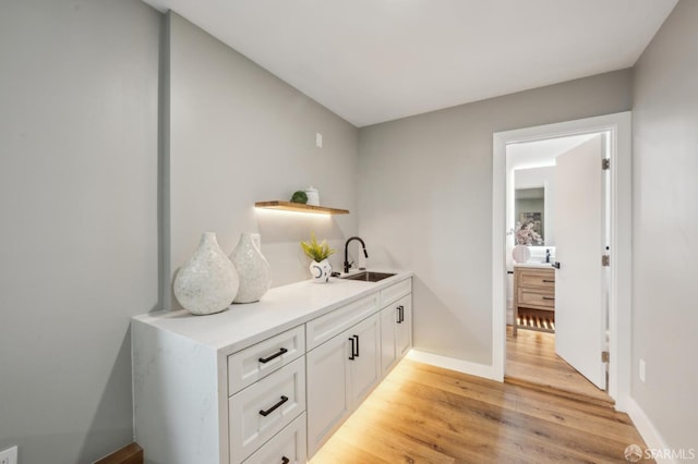 bar featuring baseboards, a sink, and light wood-style floors