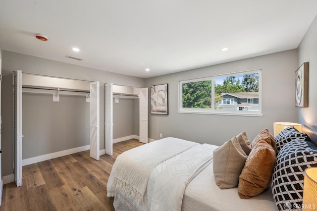 bedroom featuring wood finished floors, multiple closets, baseboards, visible vents, and recessed lighting