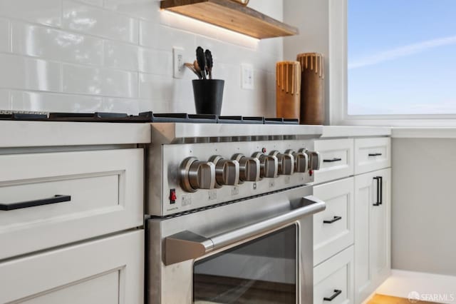 interior details with stainless steel stove, backsplash, white cabinetry, and oven
