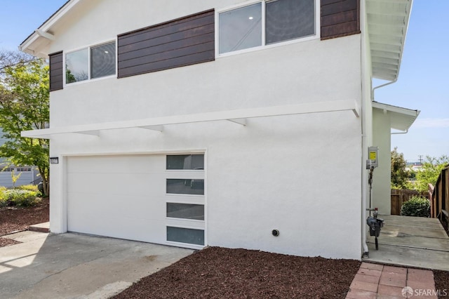view of front facade with an attached garage, concrete driveway, fence, and stucco siding