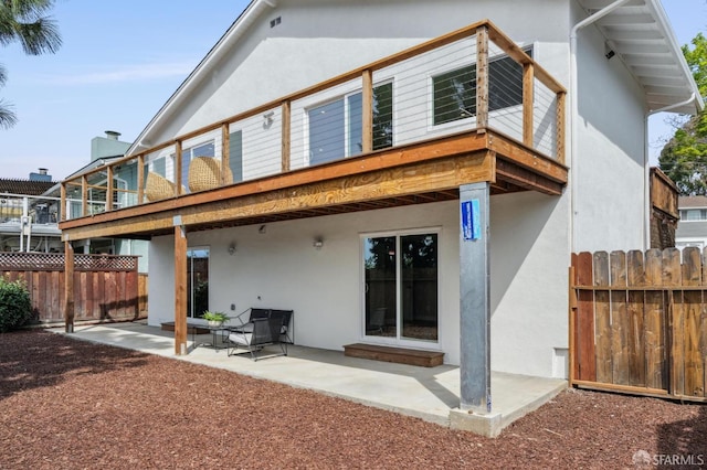 rear view of property featuring stucco siding, fence, and a patio area