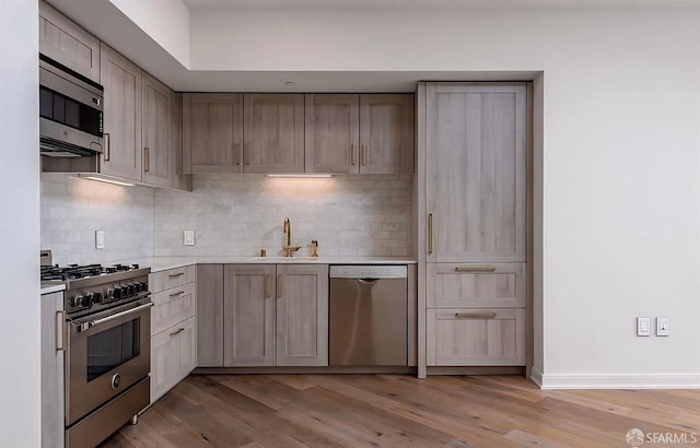 kitchen featuring a sink, light wood-style floors, light countertops, tasteful backsplash, and appliances with stainless steel finishes