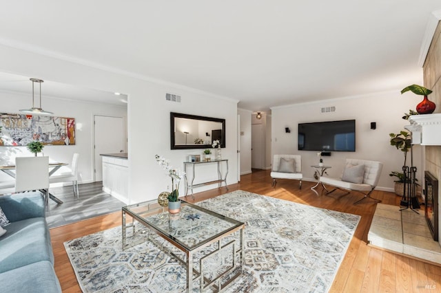 living room with a tiled fireplace, ornamental molding, and hardwood / wood-style flooring