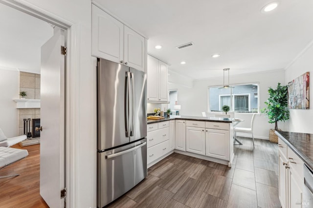 kitchen with pendant lighting, kitchen peninsula, white cabinetry, stainless steel refrigerator, and a tiled fireplace